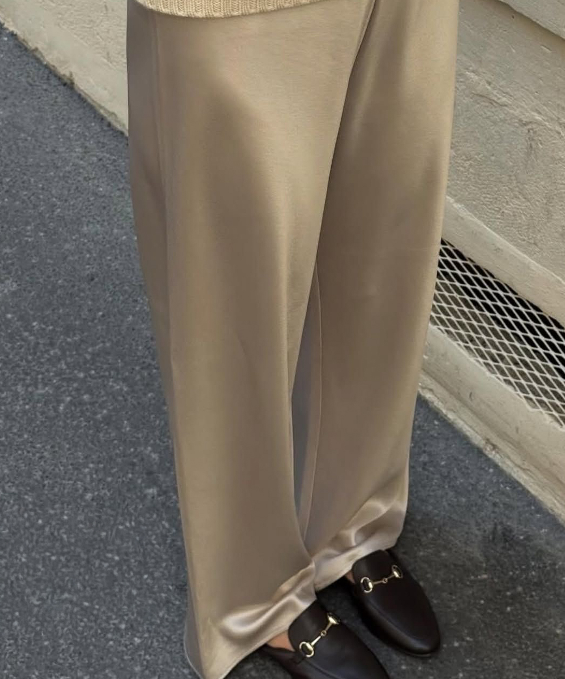 Pantalon beige à jambes larges porté avec des mocassins noirs ornés d’un détail métallique doré.