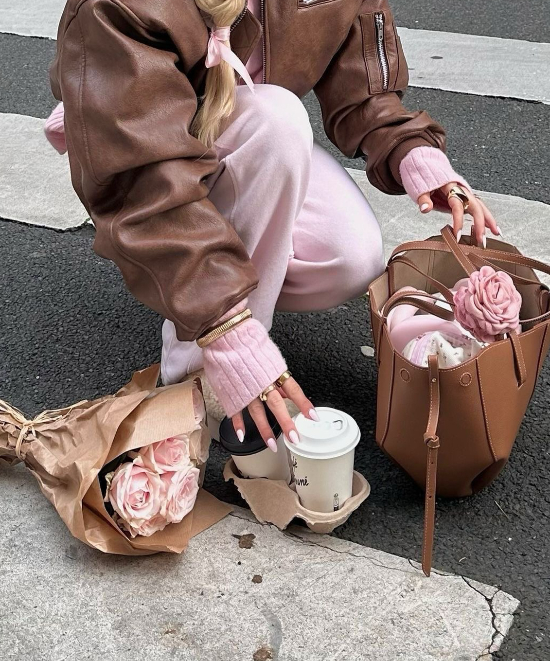 Femme portant un ensemble rose et une veste brune, avec un sac à main et un bouquet de roses