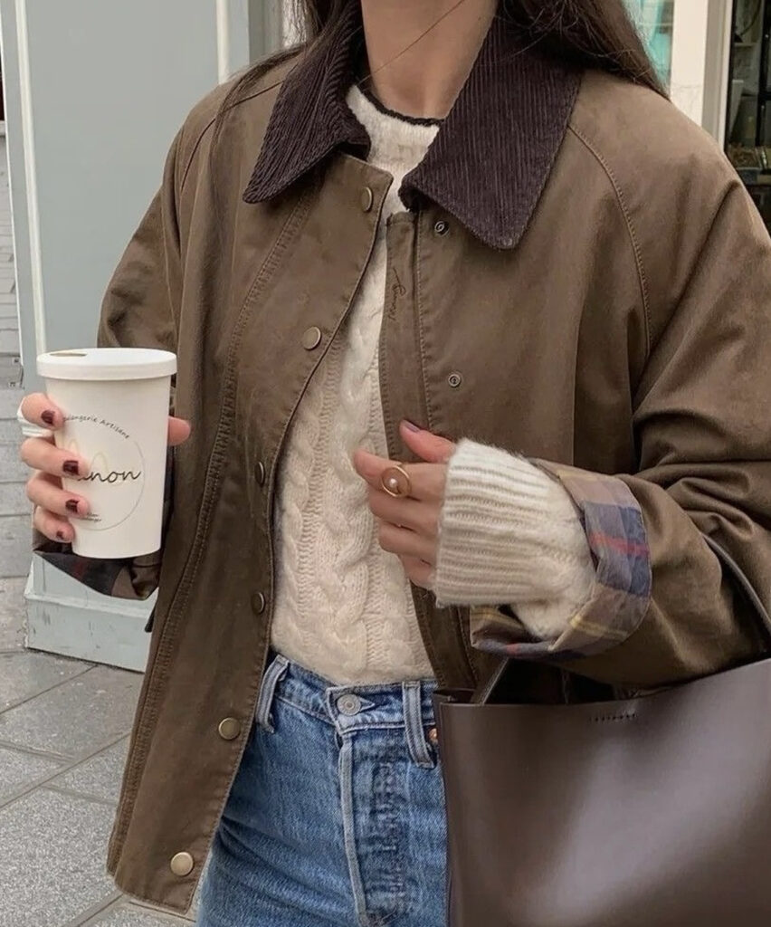 Femme portant une veste brune à col en velours, un pull crème, un jean et un sac brun.