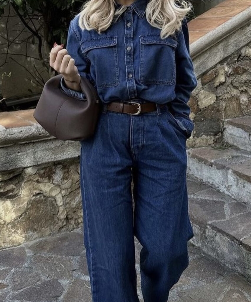 Femme portant une tenue entièrement en denim avec une chemise et un pantalon bleu, accessoirisée d’une ceinture brune et d’un sac à main.