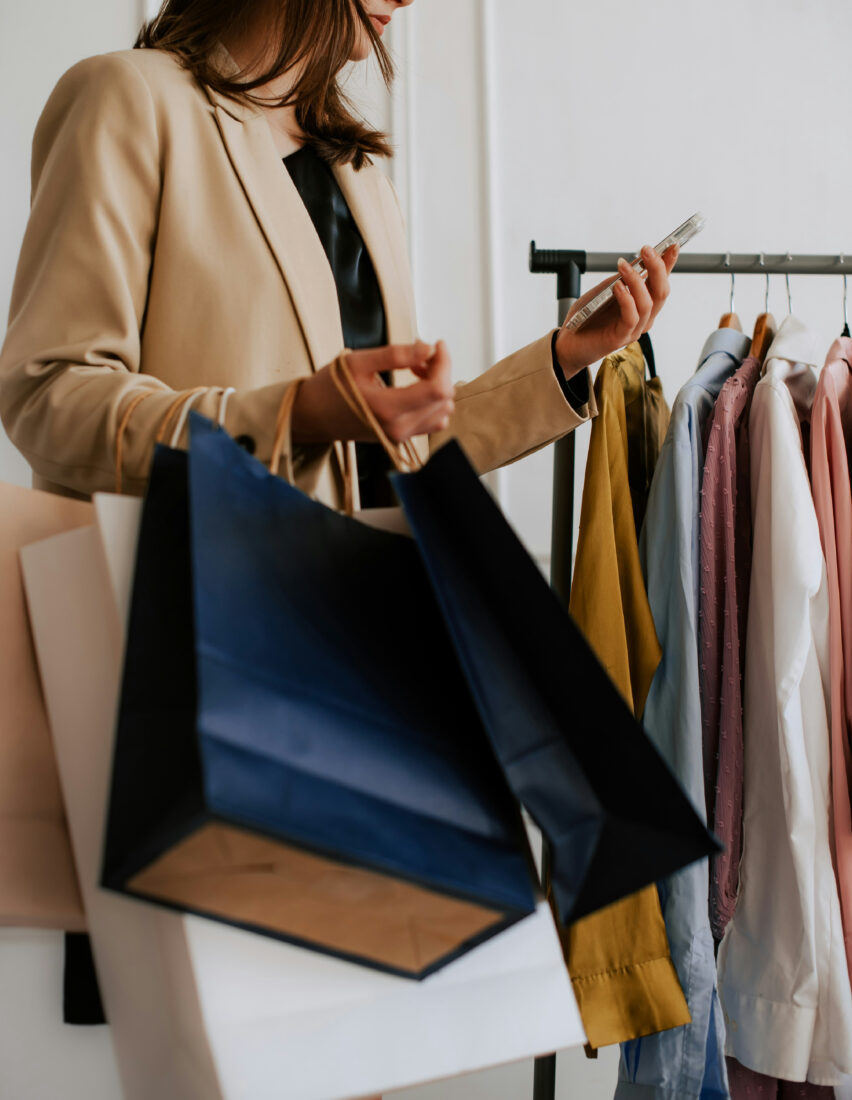 Styliste en veston beige avec des sacs de magasinage choisissant un vêtement