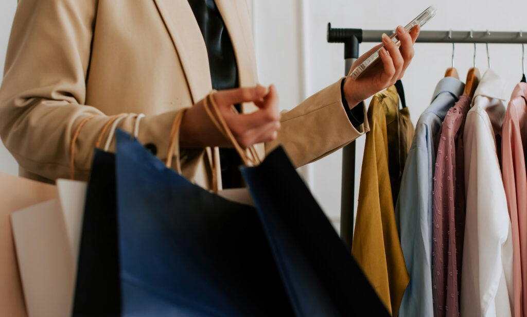 Styliste tenant des sacs de magasinage devant un portant de vêtements
